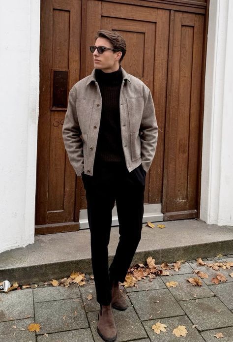 Stylish man in fall outfit with brown jacket and boots stands against wooden door with autumn leaves on the ground.
