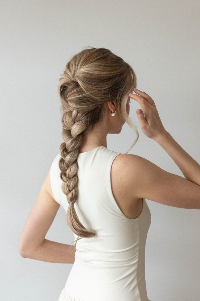 Woman with stylish long braid hairstyle, wearing a white sleeveless top, viewed from the back.