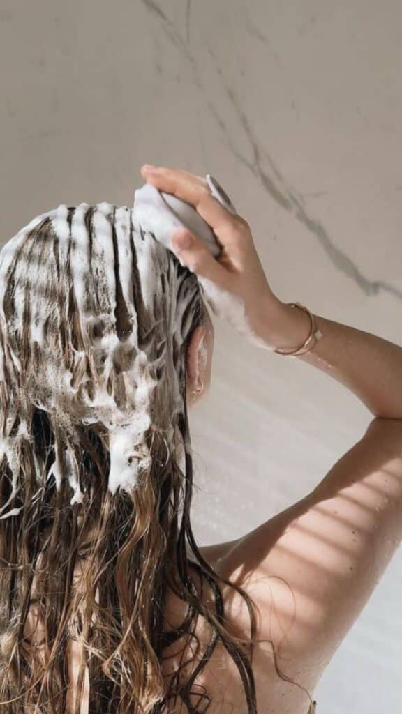 _ 15 Woman washing hair with shampoo in shower, creating rich lather. | Sky Rye Design Woman washing hair with shampoo in shower, creating rich lather.