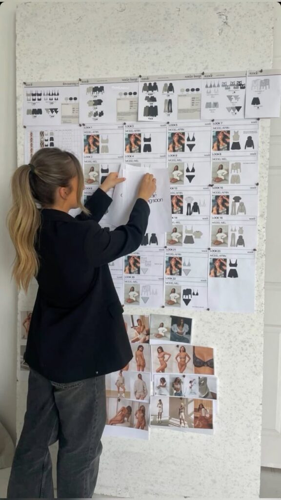Woman arranging fashion design sketches on mood board in office.