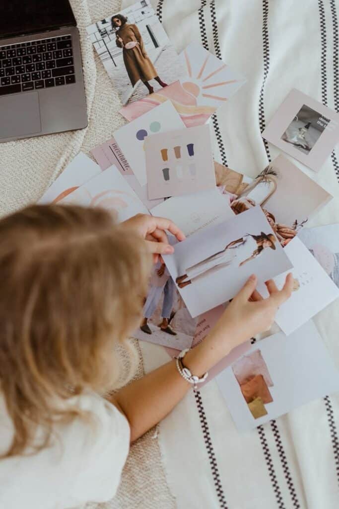 Person reviewing fashion design sketches and photos on a table with a laptop in the background.