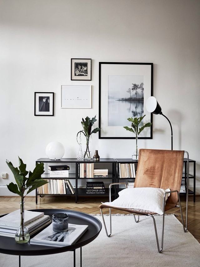 Modern living room with leather chair, art prints, and plants, featuring a minimalist design and black bookcase.