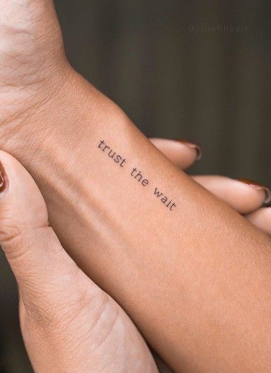 Close-up of a wrist tattoo with the phrase trust the wait held by another hand, symbolizing patience and trust.