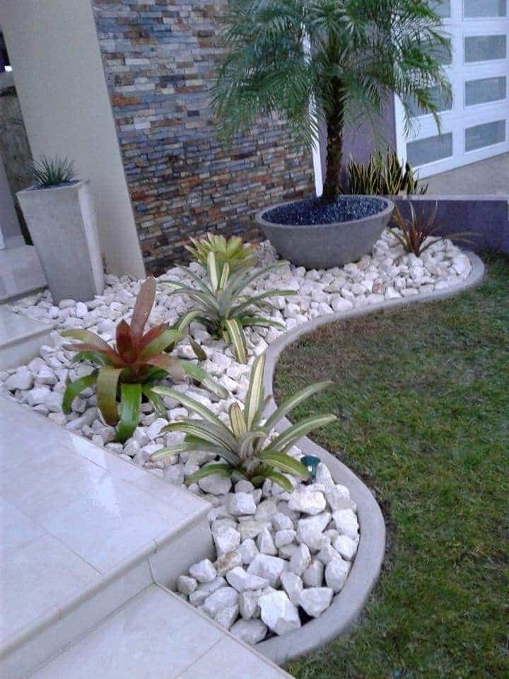 Modern garden design with white stones, tropical plants, and a palm tree in a pot beside a tiled pathway.