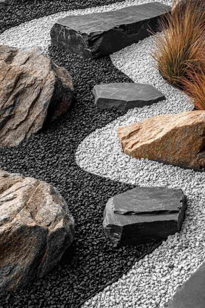 Zen garden with black and white pebbles, large stones, and grass for a calming landscape design.