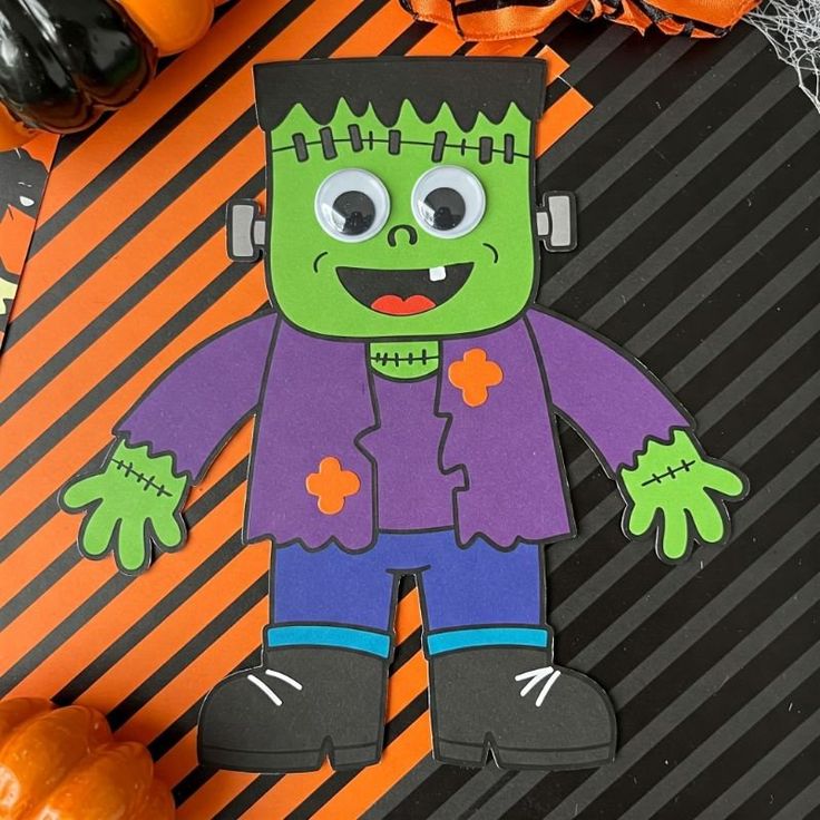 Cartoon Frankenstein Halloween decoration with googly eyes on a striped orange and black background.
