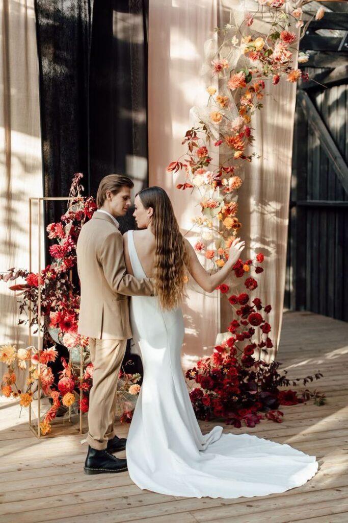 Bride and groom embrace by floral arch at rustic wedding venue.