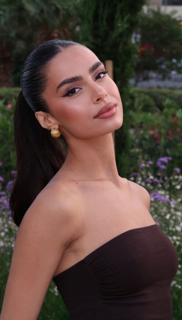 Elegant woman in a strapless dress, posing outdoors with lush greenery and flowers in the background.