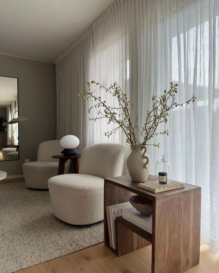 Modern living room with cozy chairs, wooden side table, vase, and sheer curtains for a minimalist and elegant design.