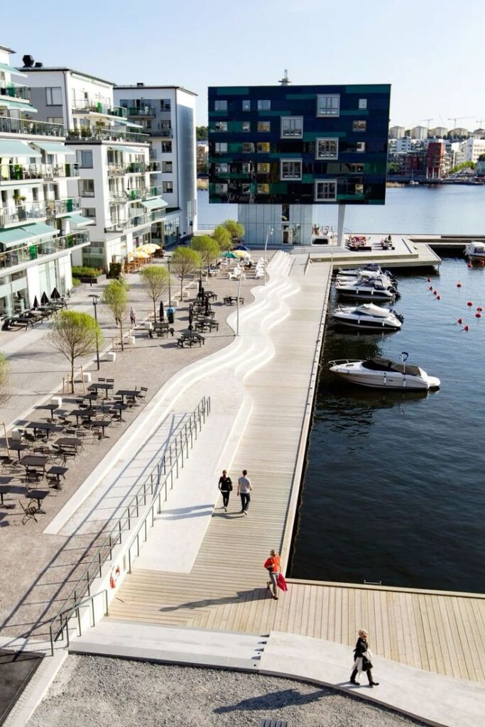 Modern waterfront architecture with boardwalk, boats, and apartments under a clear sky.
