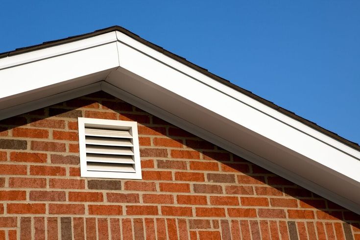 Brick house gable with roof vent and clear blue sky background.