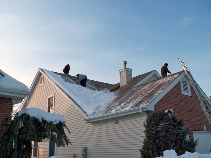 People clearing snow from a house roof in winter, ensuring roof safety and preventing ice dams.