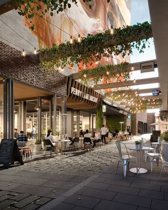 Outdoor urban cafe scene with people dining under string lights and greenery at Penny Lane Arcade.