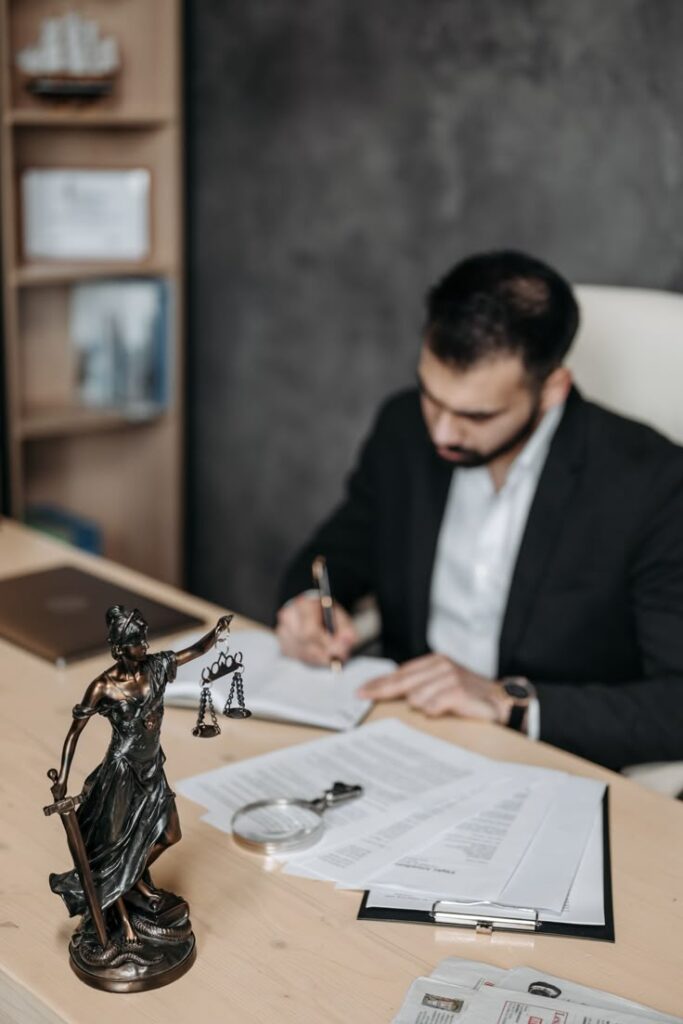 Man in office writing legal documents near Lady Justice statue.