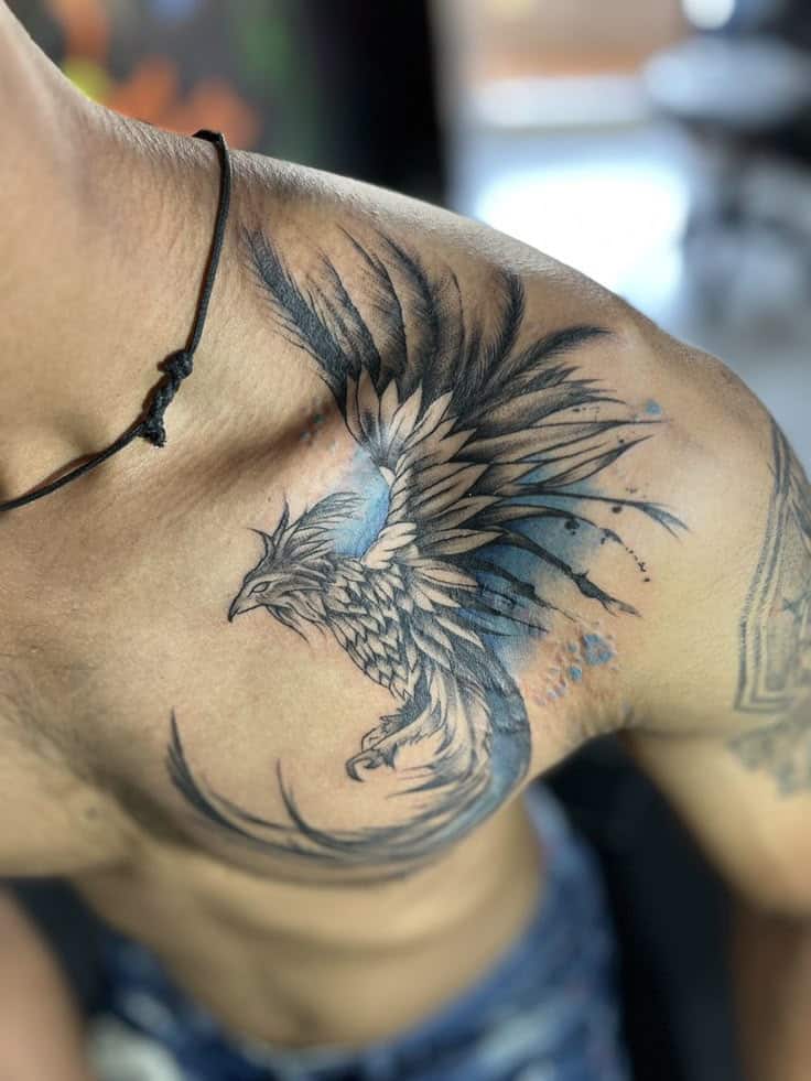 Blue and black phoenix tattoo on a person's shoulder, detailed and artistic.