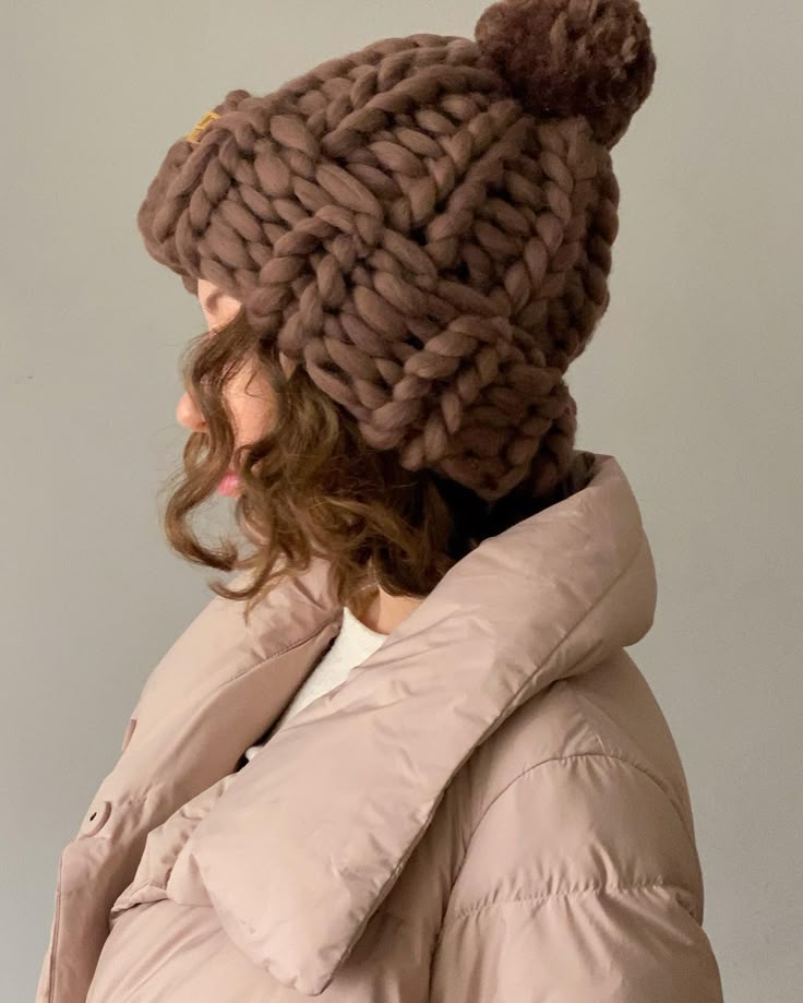 Woman wearing a chunky knit brown beanie and beige puffer jacket, showing cozy winter fashion.