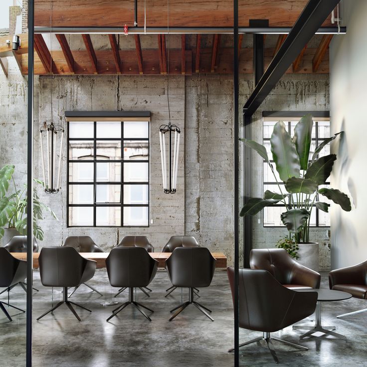 Modern industrial office with leather chairs, large windows, and indoor plants for a stylish workspace.