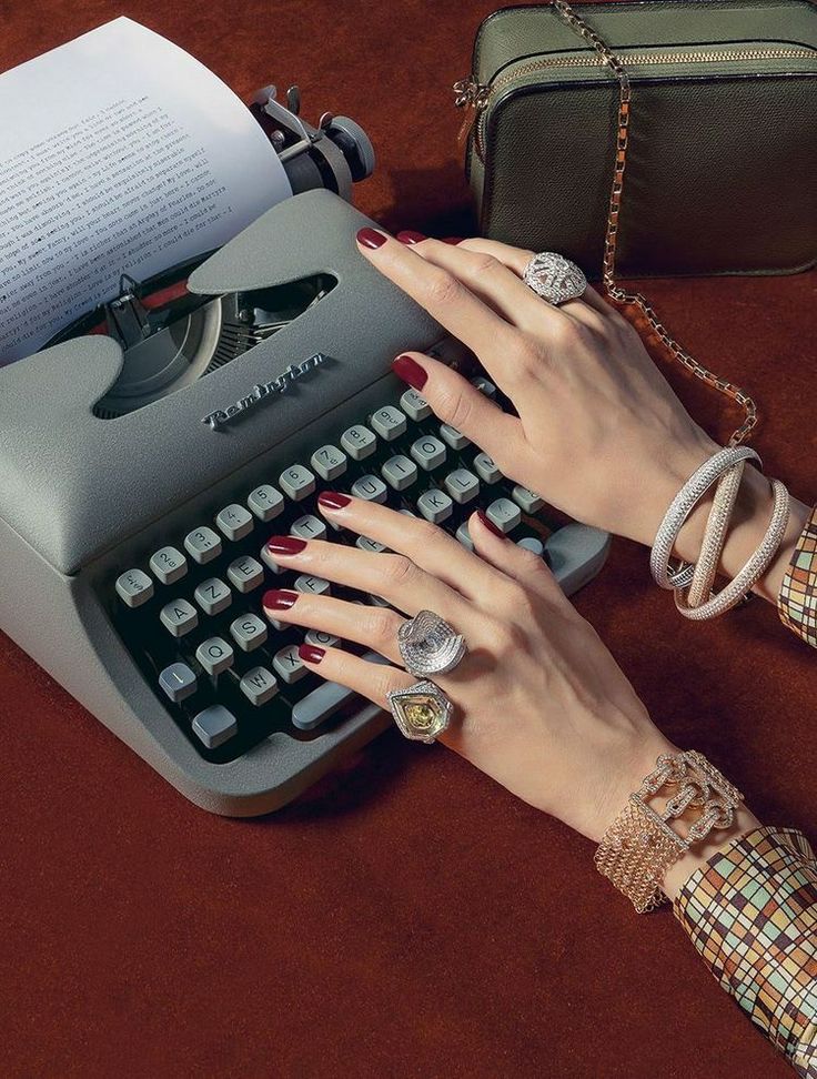 Elegant hands with jewelry type on a vintage typewriter, over a brown background with accessories.