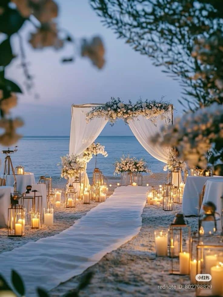 Beachfront wedding setup at sunset with candles and a floral archway.