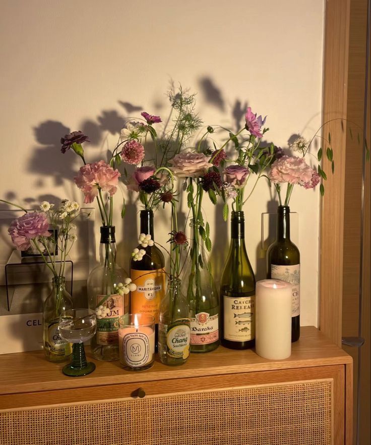 Floral arrangement in upcycled bottles with candles on a wooden shelf, creating a cozy, decorative atmosphere.