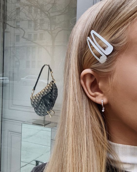_ 18 Close-up of woman with white hair clips and earrings, luxury handbag displayed in store window in background. | Sky Rye Design Close-up of woman with white hair clips and earrings, luxury handbag displayed in store window in background.