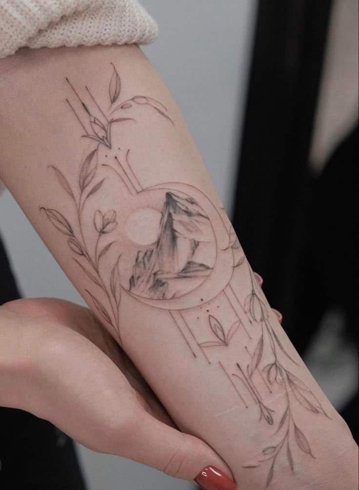 Minimalist mountain tattoo with floral elements on forearm, showcasing nature-inspired art and delicate line work.