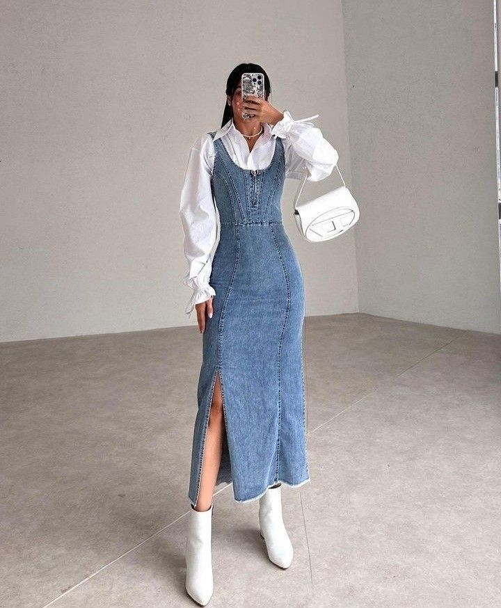 Stylish woman in a denim dress, white blouse, and boots takes a mirror selfie; chic and modern fashion look.