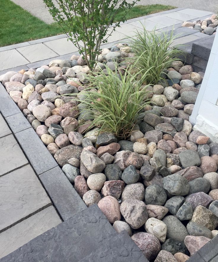Modern landscape design with decorative rocks and plants in a neatly bordered garden bed.