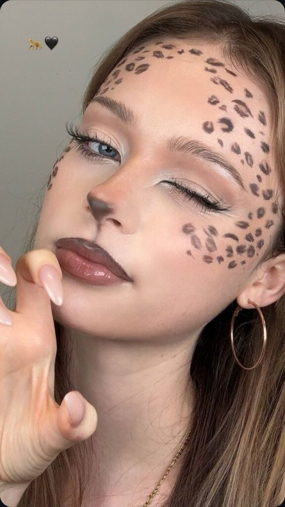 Woman with leopard makeup winking, showcasing creative Halloween costume with animal print face design.