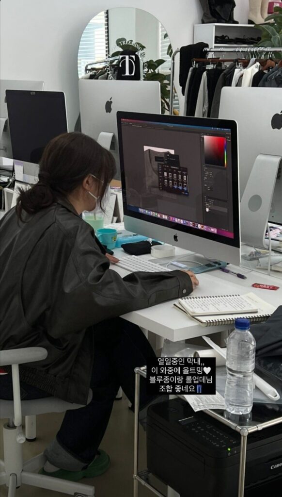 Person working on a computer at a desk with notebooks and a water bottle nearby in an office setting.
