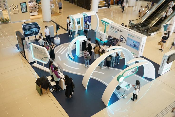 Interactive tech exhibit in shopping mall with attendees exploring futuristic displays and information booths.