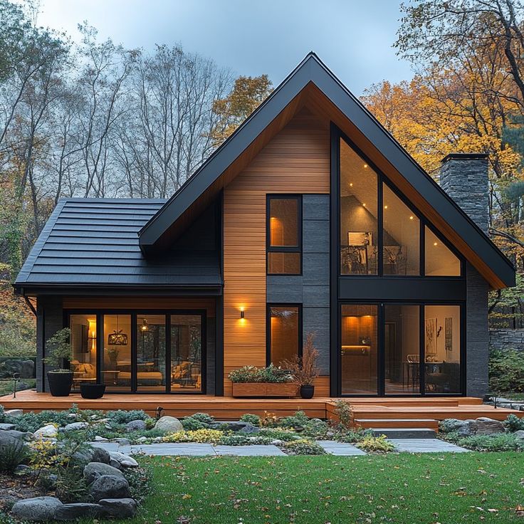 Modern A-frame house with large windows and wooden deck, surrounded by autumn trees and lush garden landscape.