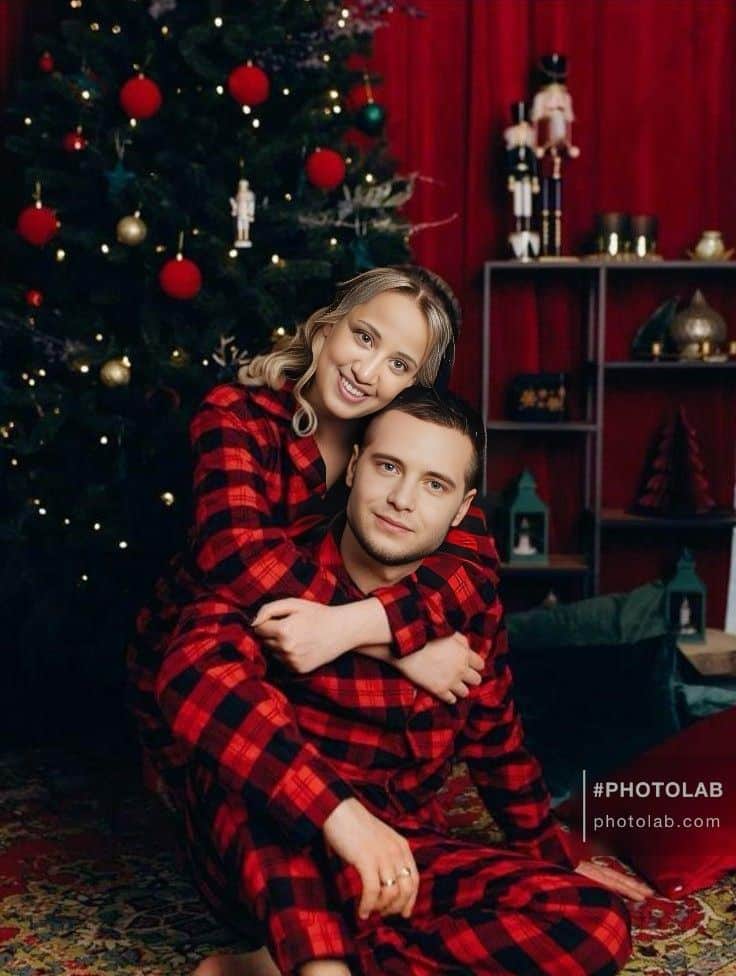 Couple in matching red plaid pajamas by a Christmas tree, creating a festive holiday atmosphere.