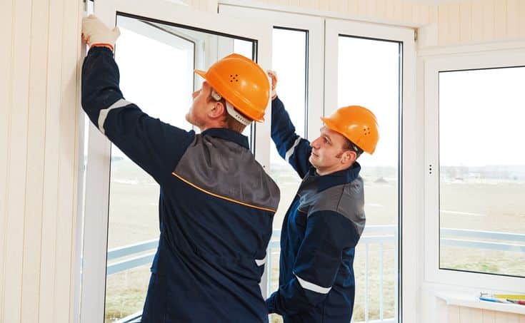 Two workers in hard hats installing large windows in a building, ensuring proper fit and alignment for energy efficiency.