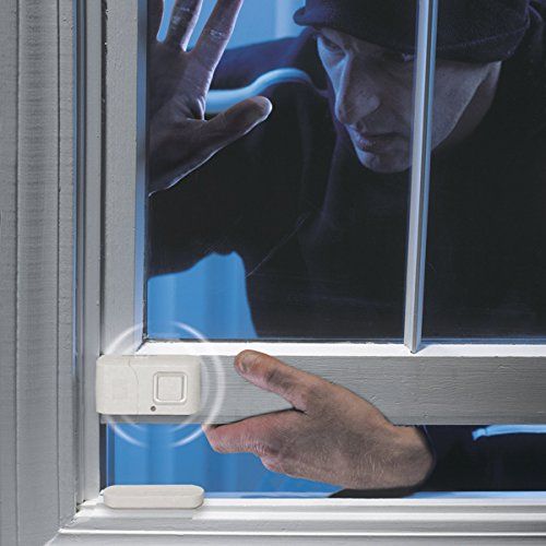 Burglar attempting to open a window protected by a security alarm system at night.