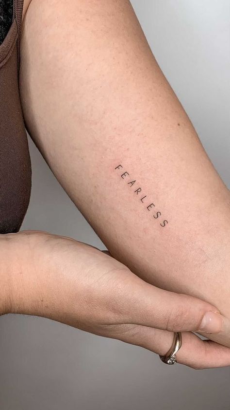 Minimalist 'Fearless' tattoo on forearm, vertical lettering, inspirational body art, close-up view.