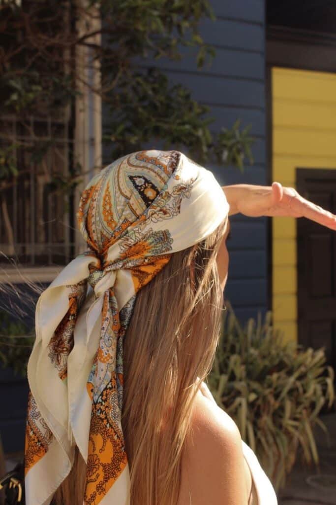 Edited in Tezza with Cocoa Person in printed headscarf shielding eyes from sun, standing outside in front of colorful house. | Sky Rye Design Person in printed headscarf shielding eyes from sun, standing outside in front of colorful house.