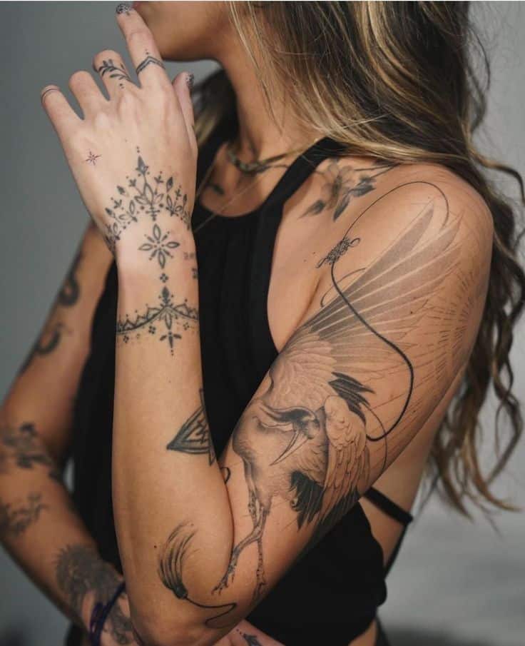 Woman with intricate bird and floral tattoos on arm and hand, wearing a black top, showcasing artistic body art.