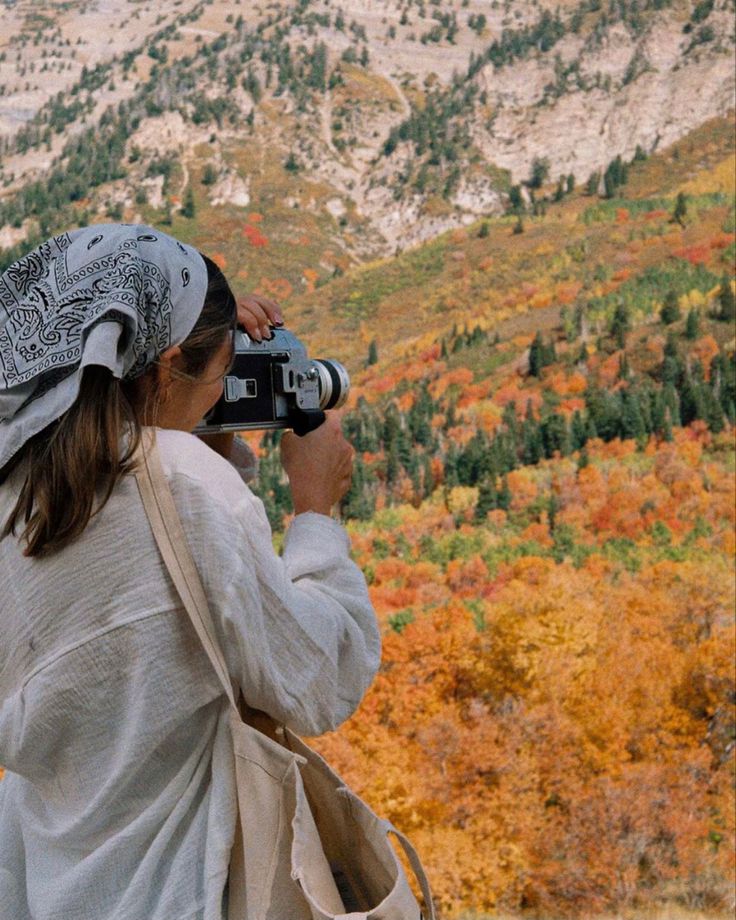 Person capturing vibrant autumn landscape with a vintage camera in a mountainous area.
