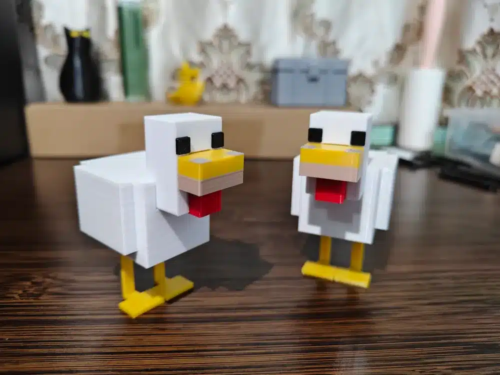 3D printed pixelated chickens on a wooden table, with a blurred decorative background.