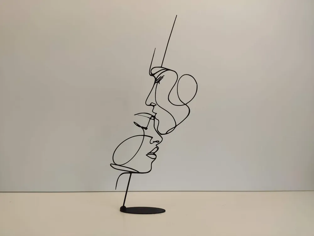 Minimalist wire sculpture of two abstract faces on a plain background.