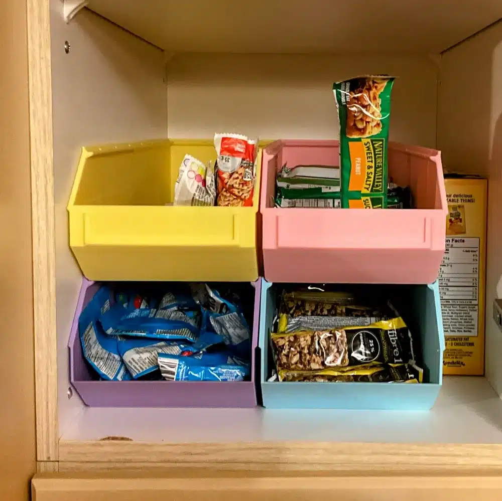 Organized pantry shelf with colorful bins storing assorted snack bars.
