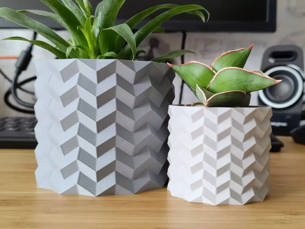 Two geometric-patterned plant pots with succulents on a wooden desk.