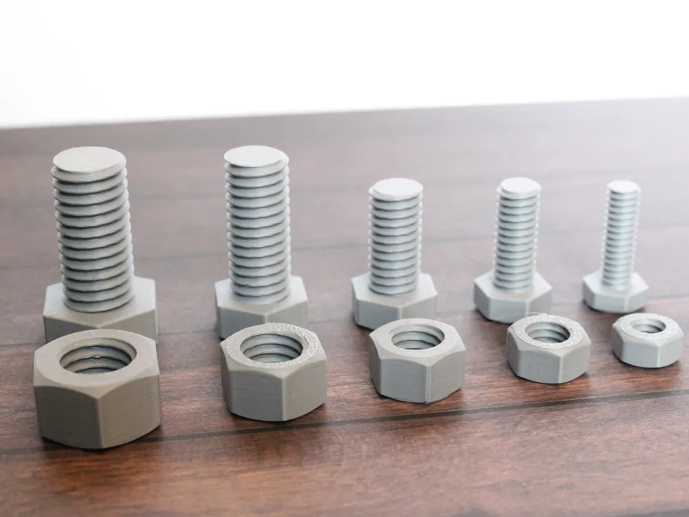 3D-printed gray nuts and bolts in various sizes on wooden surface.