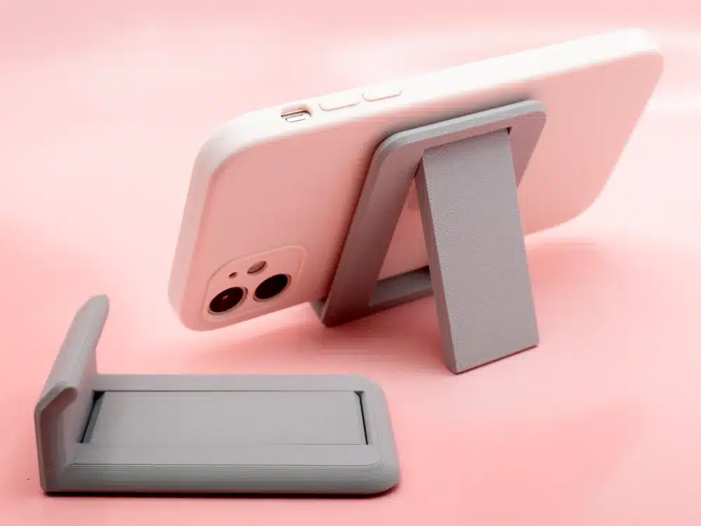 Phone with stand on pink background, showcasing a compact, foldable design for convenient support and viewing.