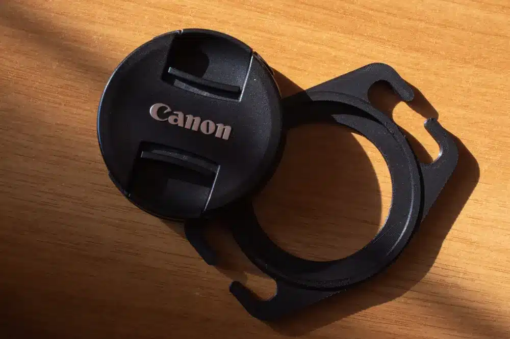 Canon lens cap and holder on wooden surface, close-up view with natural light.