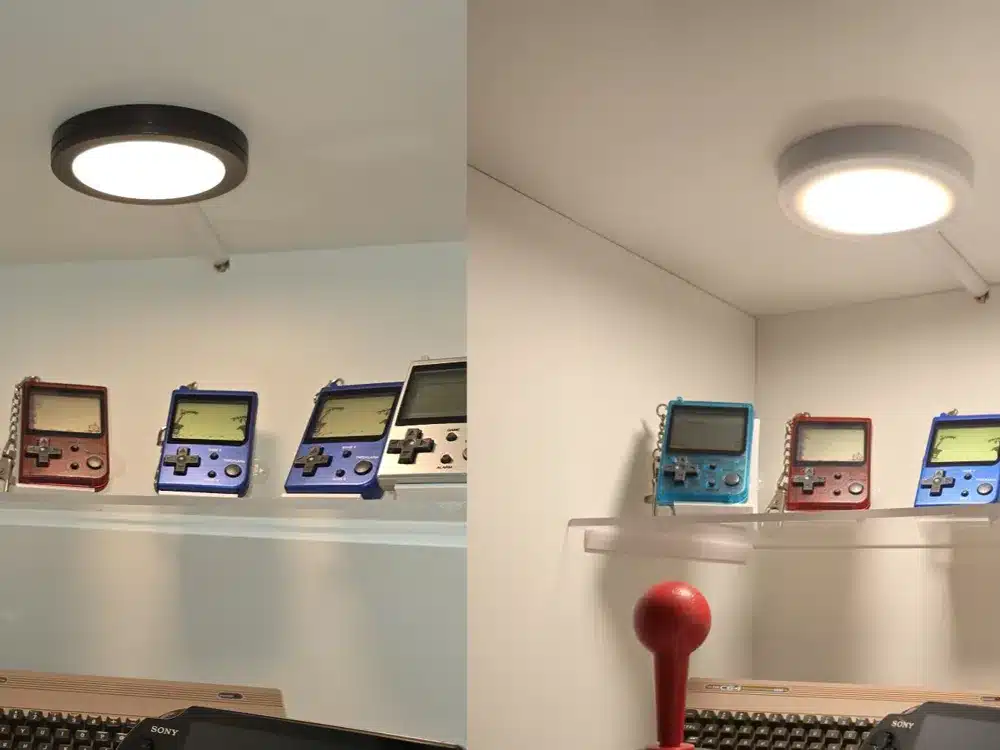 Two ceiling lights illuminate a display shelf with vintage handheld gaming devices.