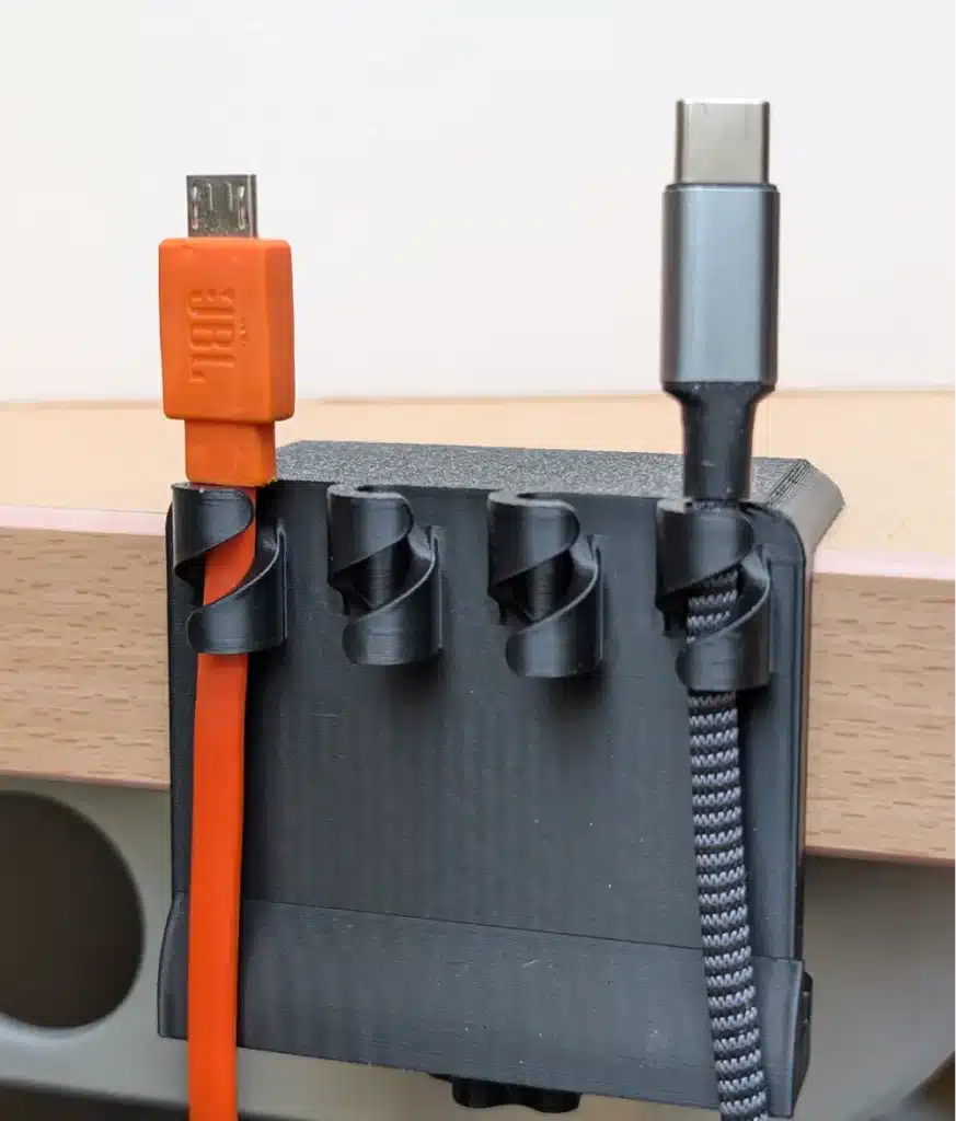 Cable organizer with orange micro USB and black USB-C cables neatly arranged on a desk edge.