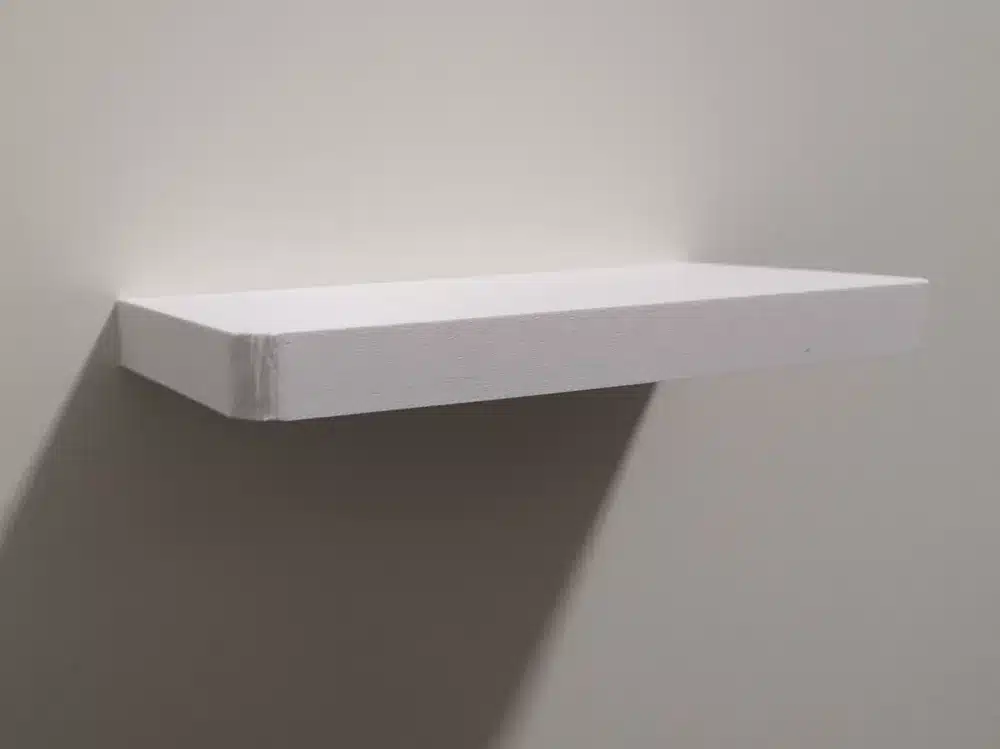 Minimalist white floating shelf mounted on a plain wall, casting a shadow.