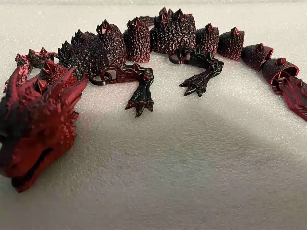 Red and black 3D-printed dragon model with textured scales on a white surface.
